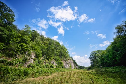 Valley with green fields under a blue sky with cliffs on the side on a summer day