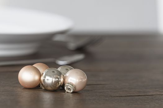 Christmas baubles in elegant colors on a dinner table with dish in the background