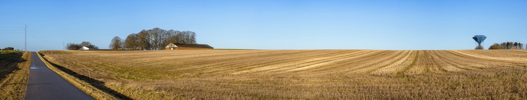 Rural panorama landscape with a dry field under a blue sky with a water tower on the right side