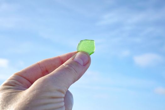 Hand holding green sanded glass up against a blue sky on an ocean shore