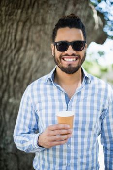 Handsome man in sunglasses holding disposable coffee cup in the park on a sunny day
