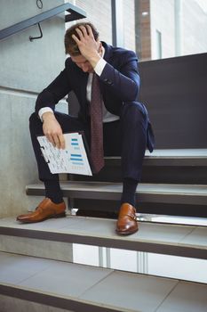 Depressed businessman with clipboard sitting on stairs at office