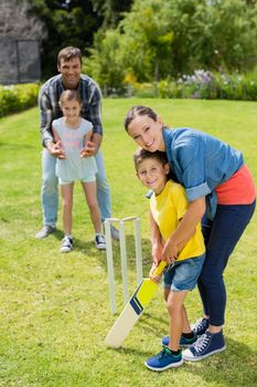 Family playing cricket in park on a sunny day