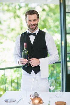 Portrait of male waiter holding bottle of wine in restaurant