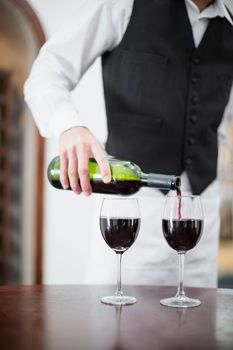 Mid-section of male waiter pouring wine in wine glasses