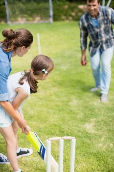 Family playing cricket in park on a sunny day