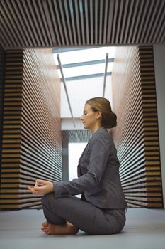Businesswoman performing yoga in the corridor at office