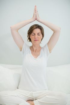 Woman doing meditation on bed in bedroom at home