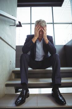 Depressed businessman sitting with hand on head at office