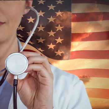 Close-up of female doctor holding stethoscope against american flag against sky during sunset