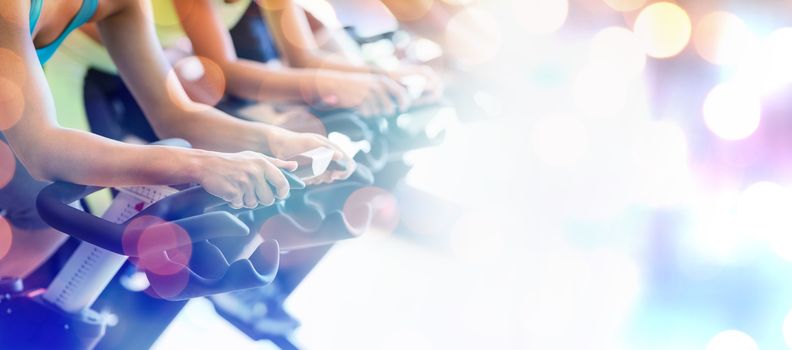 Glowing background against cropped image of people in spin class