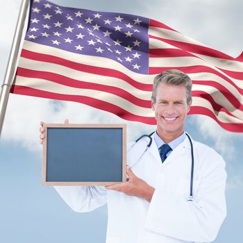 Portrait of smiling male doctor holding blank slate against composite image of low angle view of american flag