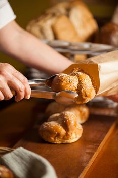 Hands of female staff packing sweet food in paper bag at supermarket