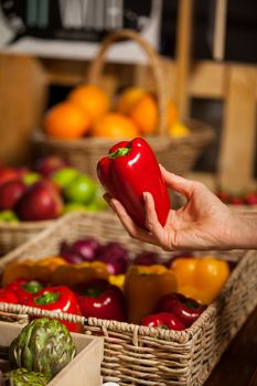 Hand of female costumer holding bell pepper in organic section of supermarket