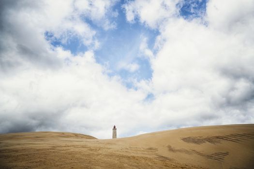 Lighthouse tower rising up on a dune beach under a cloudy blue sky