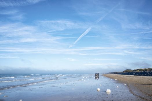 Horseback riders on a beach in the summer under a blue sky with white clouds