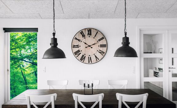 Retro clock over a table on a wall in a living room with green trees outside in the spring