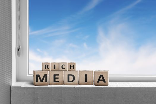 Rich media sign written on wooden blocks in a window with a blue sky outside