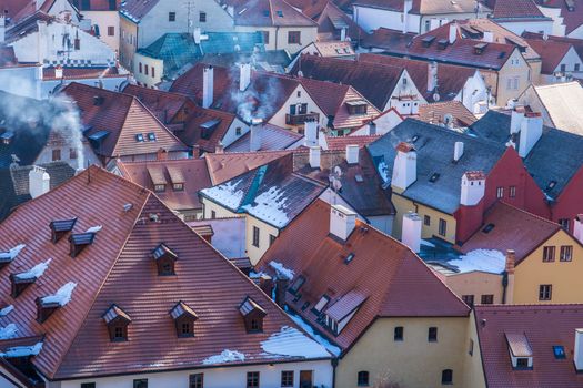 Aerial cityscape view of Cesky Krumlov Old Town on winter day. Snow covered rooftops from tiles, Smoke from chimneys on cold day.