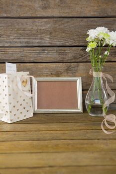 Close-up of gift bag, photo frame and flower vase on wooden surface