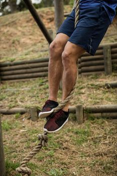Low section of man climbing a rope during obstacle course in boot camp