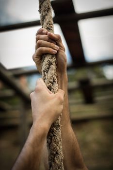 Hands of man climbing a rope during obstacle course