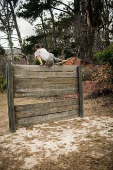 Rear view of soldier climbing wooden wall in boot camp