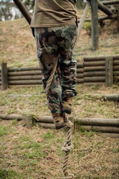 Low section of man climbing a rope during obstacle course in boot camp