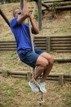 Fit man climbing a rope during obstacle course in boot camp