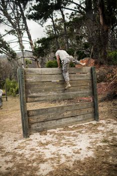 Rear view of soldier climbing wooden wall in boot camp