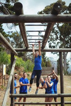 Fit woman climbing monkey bars while fit people cheering in background