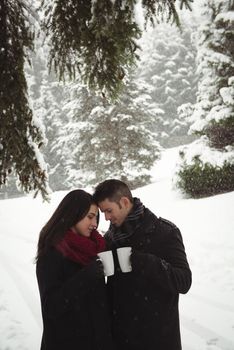 Romantic couple having cup of coffee in winter forest 