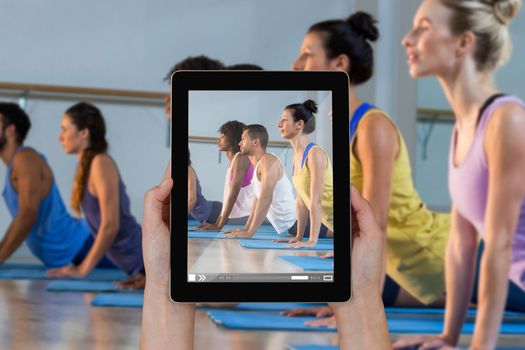 Close-up of hands holding digital tablet against group of people performing yoga
