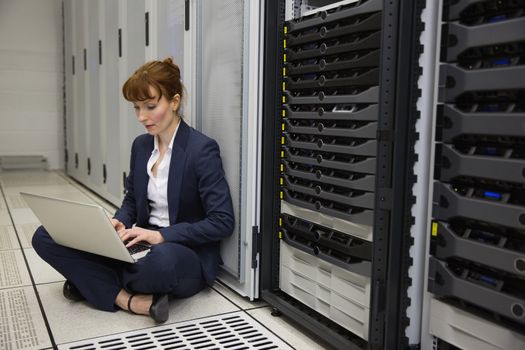 Technician sitting on floor beside server tower using laptop in large data center