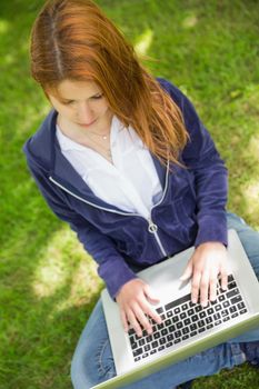 Pretty redhead relaxing in the park using laptop on a sunny day
