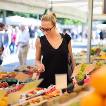 Woman buying fruits and vegetables at local food market. Market stall with variety of organic vegetable.