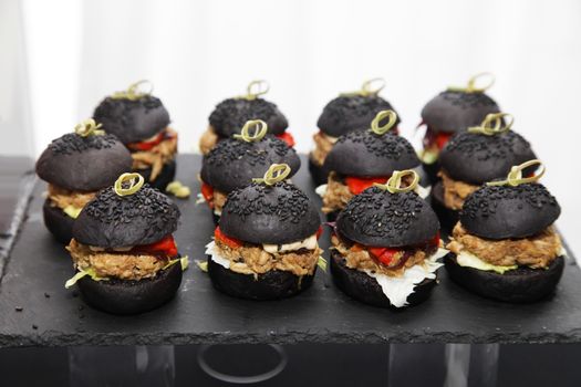 Mini burgers with black bun, stuffed with beef and tomato, sprinkled with black sesame seeds