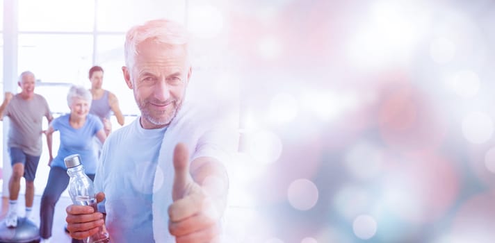 Man showing thumbs up sign with people exercising in background at fitness studio