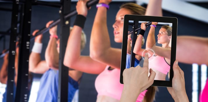 Hands touching digital tablet against white background against people doing chin ups exercise in gym