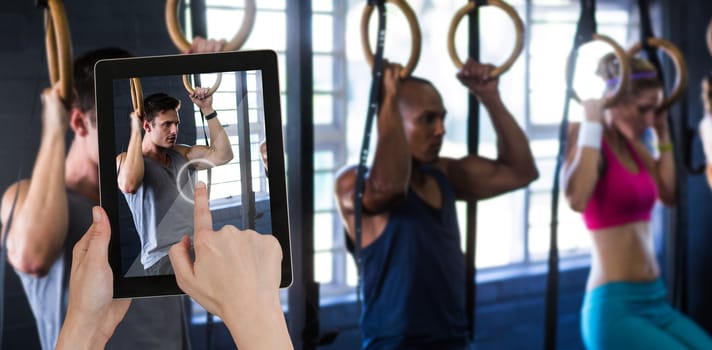 Hands touching digital tablet against white background against people hanging from gymnastic rings in gym