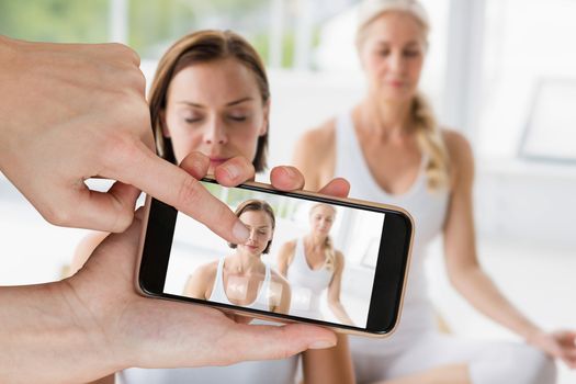Hands touching smart phone against women with eyes closed doing yoga