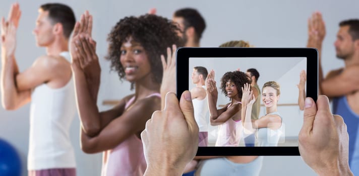 Cropped hand holding digital tablet against portrait of group of people exercising
