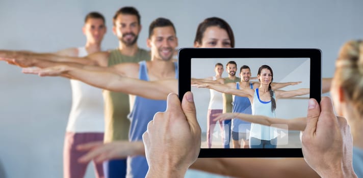 Cropped hand holding digital tablet against instructor taking yoga class