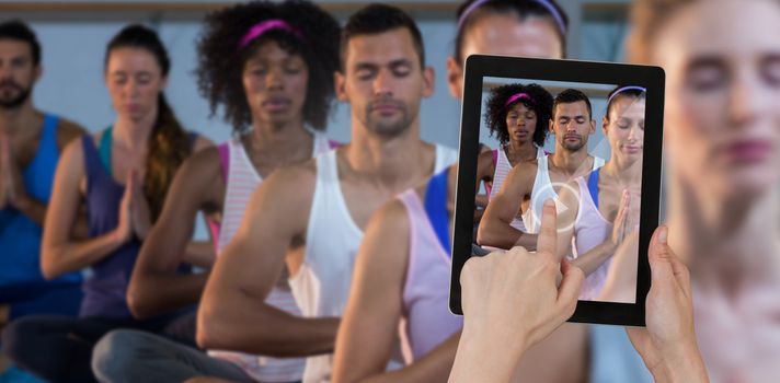Hands touching digital tablet against white background against group of people performing yoga