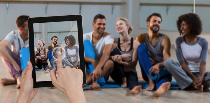 Hands touching digital tablet against white background against group of people sitting on floor