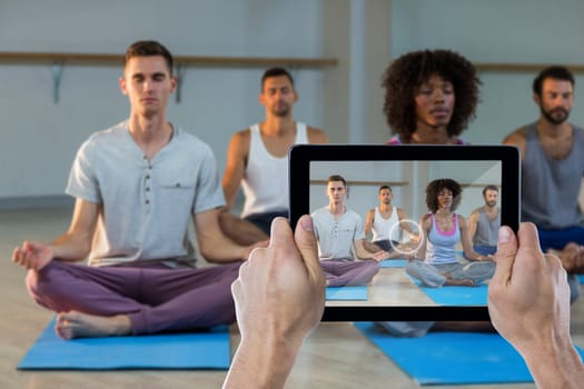 Cropped hand holding digital tablet against group of people performing yoga