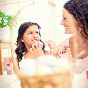 Happy mother and daughter painting easter eggs in the living room