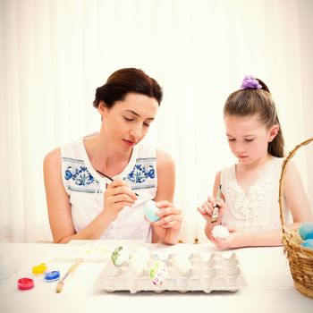 Mother and daughter painting easter eggs at home in the living room