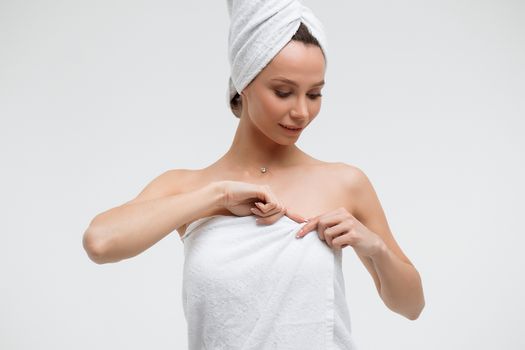 Sensual woman in fluffy white towel on head looking at finger touching towel on body