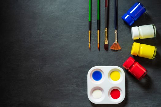 Palette and poster color bottle with paint brush on black cement background. Top view and copy space.